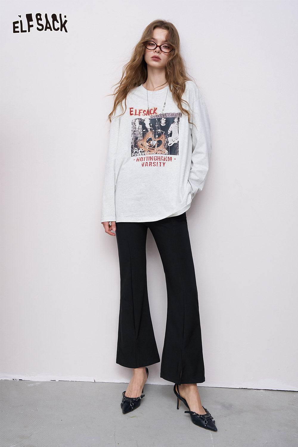 ELFSACK model wearing women's ankle-length flared pants in black with oversized graphic sweatshirt and heels