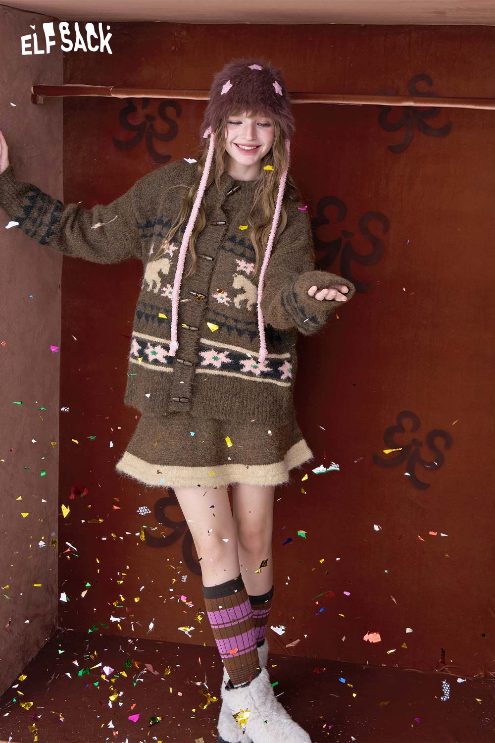 Young woman wearing a cozy ELFSACK sweater with festive details and colorful confetti, showcasing a minimalist Christmas stripe dress