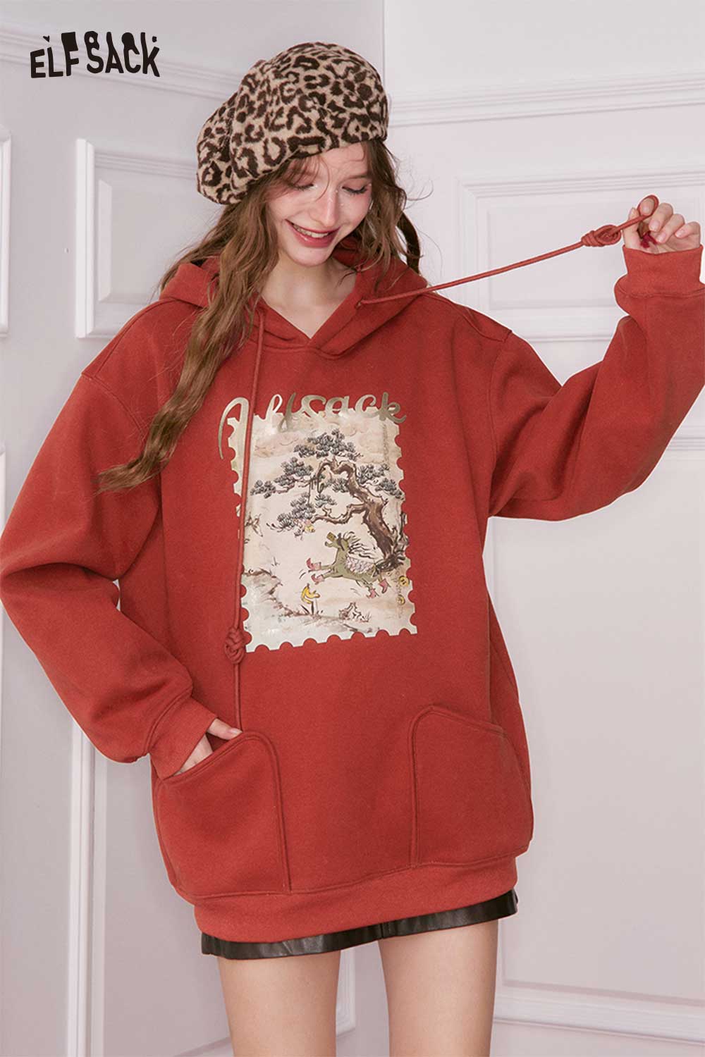 ELFSACK minimalist graphic hooded sweatshirt in rust color with a unique art design on the front
