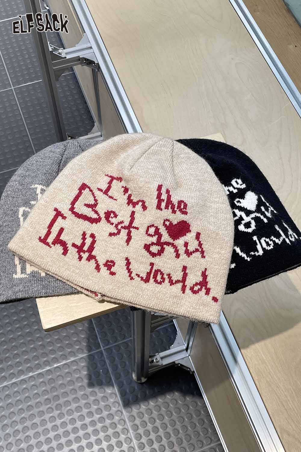 Three minimalist letter graphic beanies in beige, gray, and black with playful text designs