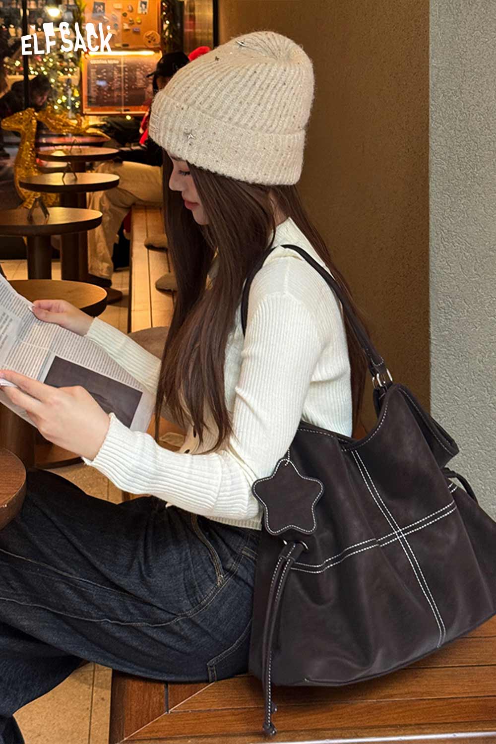 Woman sitting at a café with a minimalist PU leather shoulder bag, wearing a cozy beanie and casual outfit