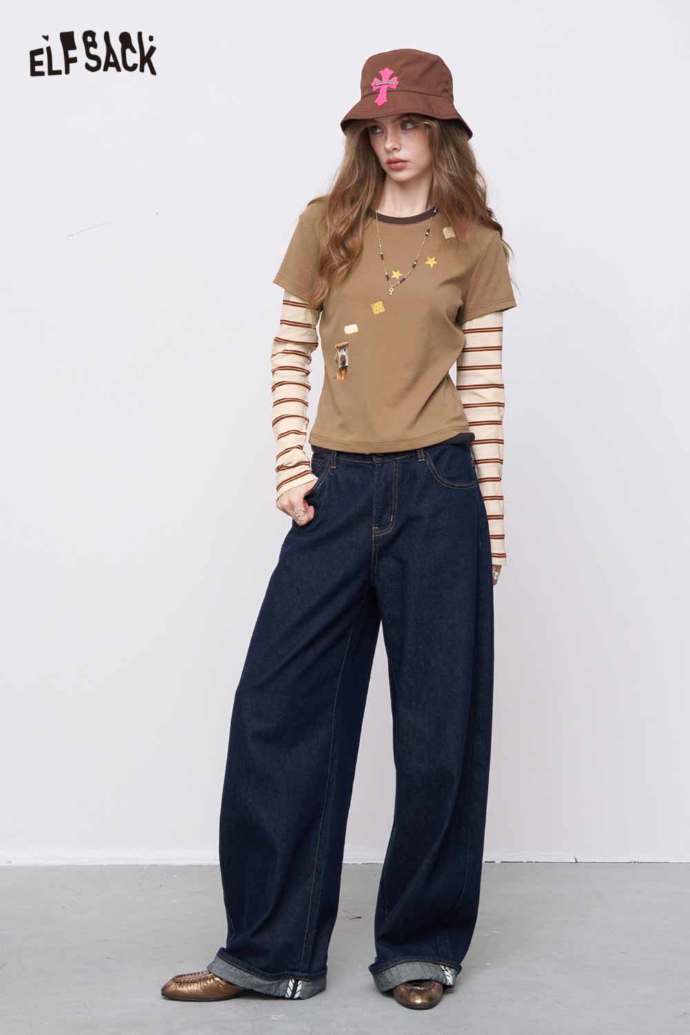 ELFSACK model wearing slim fit stripe patchwork top layered over cream striped sleeves with wide leg jeans and bucket hat