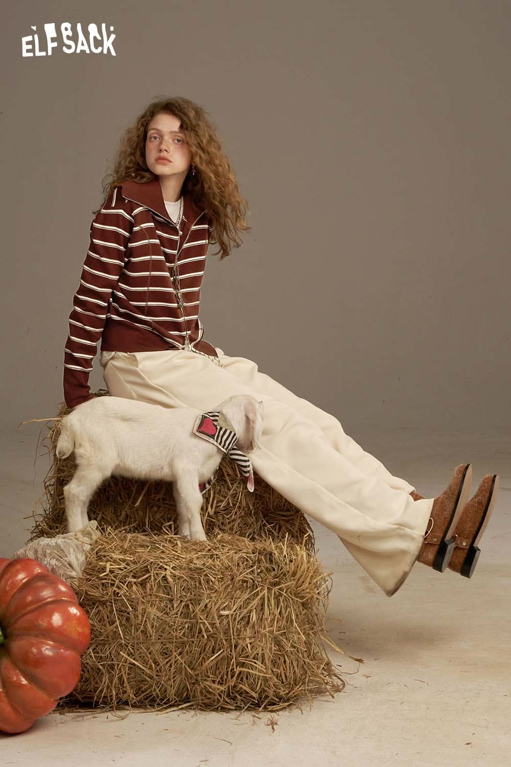 Model wearing a navy collar striped knitted cardigan paired with cream pants, sitting on a haystack