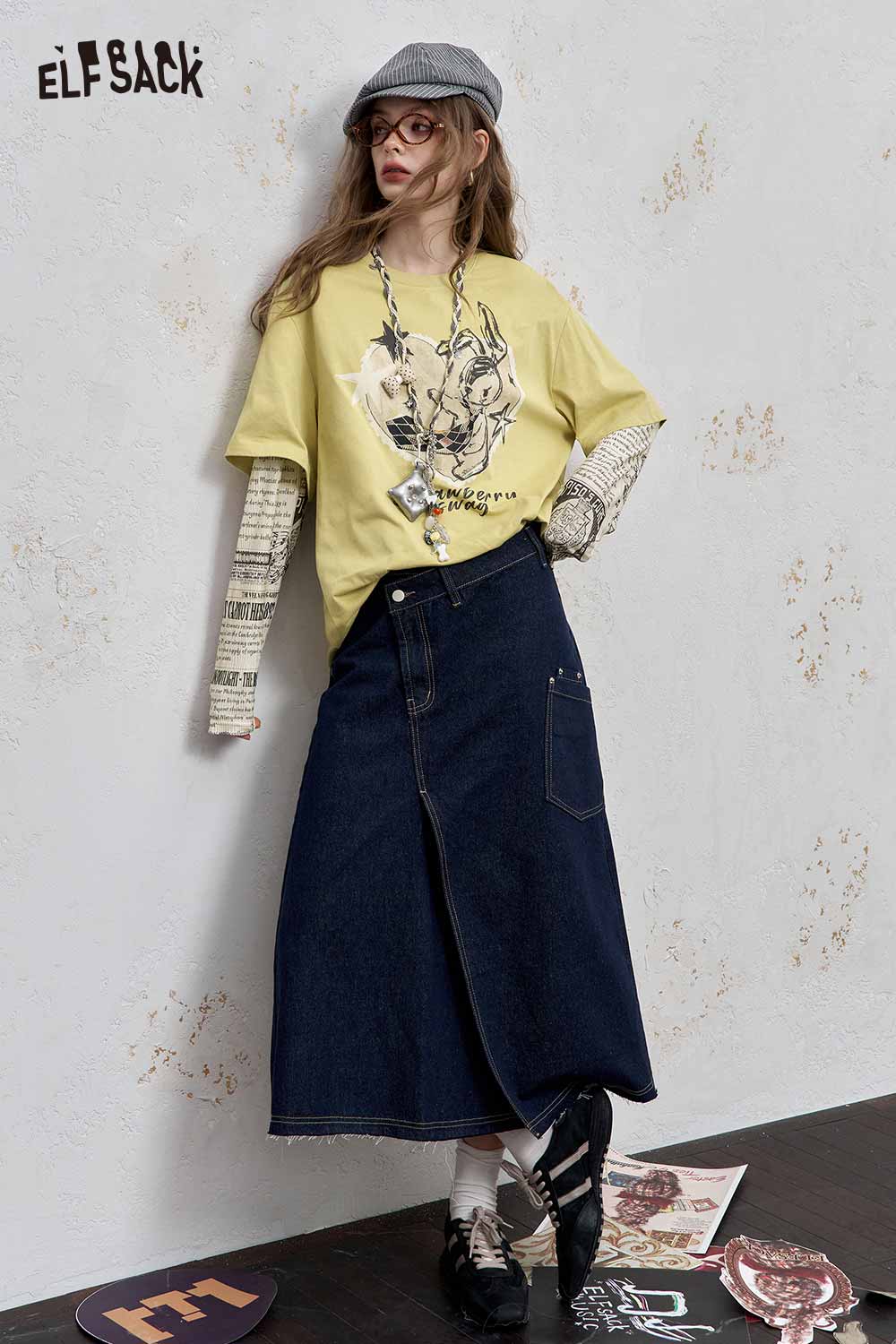 ELFSACK newsprint graphic drop shoulder tee in yellow with artistic design paired with a denim skirt