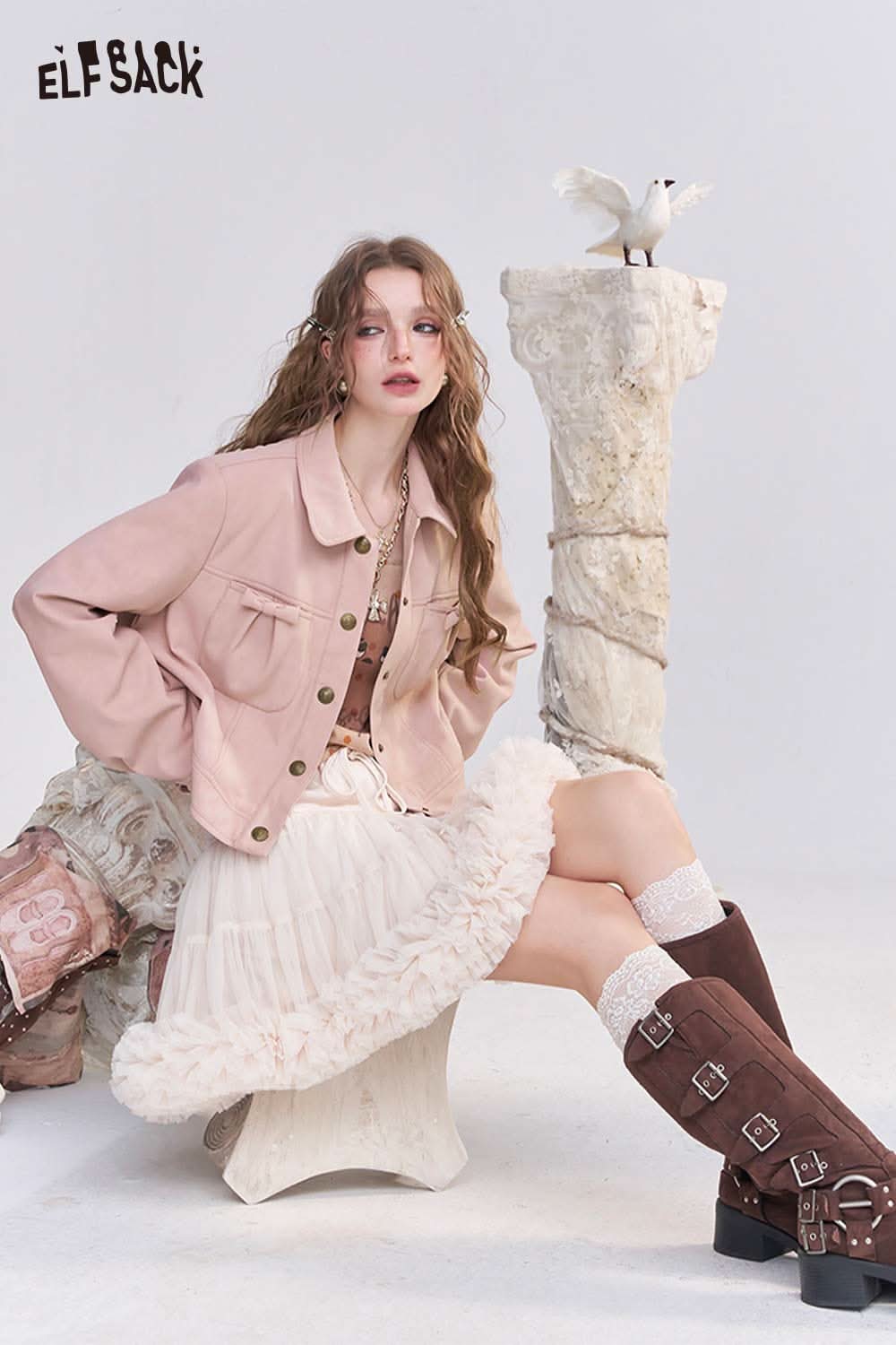 Stylish model wearing a pink faux leather motocross jacket with a ruffled skirt and knee-high boots