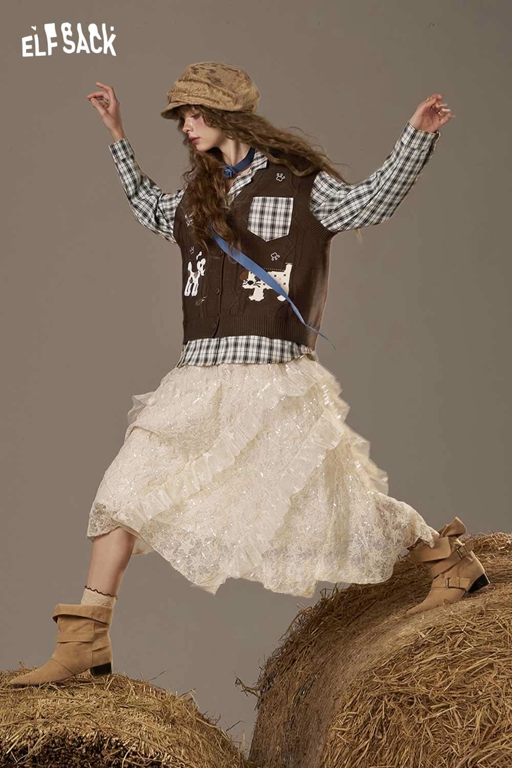 Model wearing a playful embroidered knit top layered with a brown vest and a ruffled white skirt