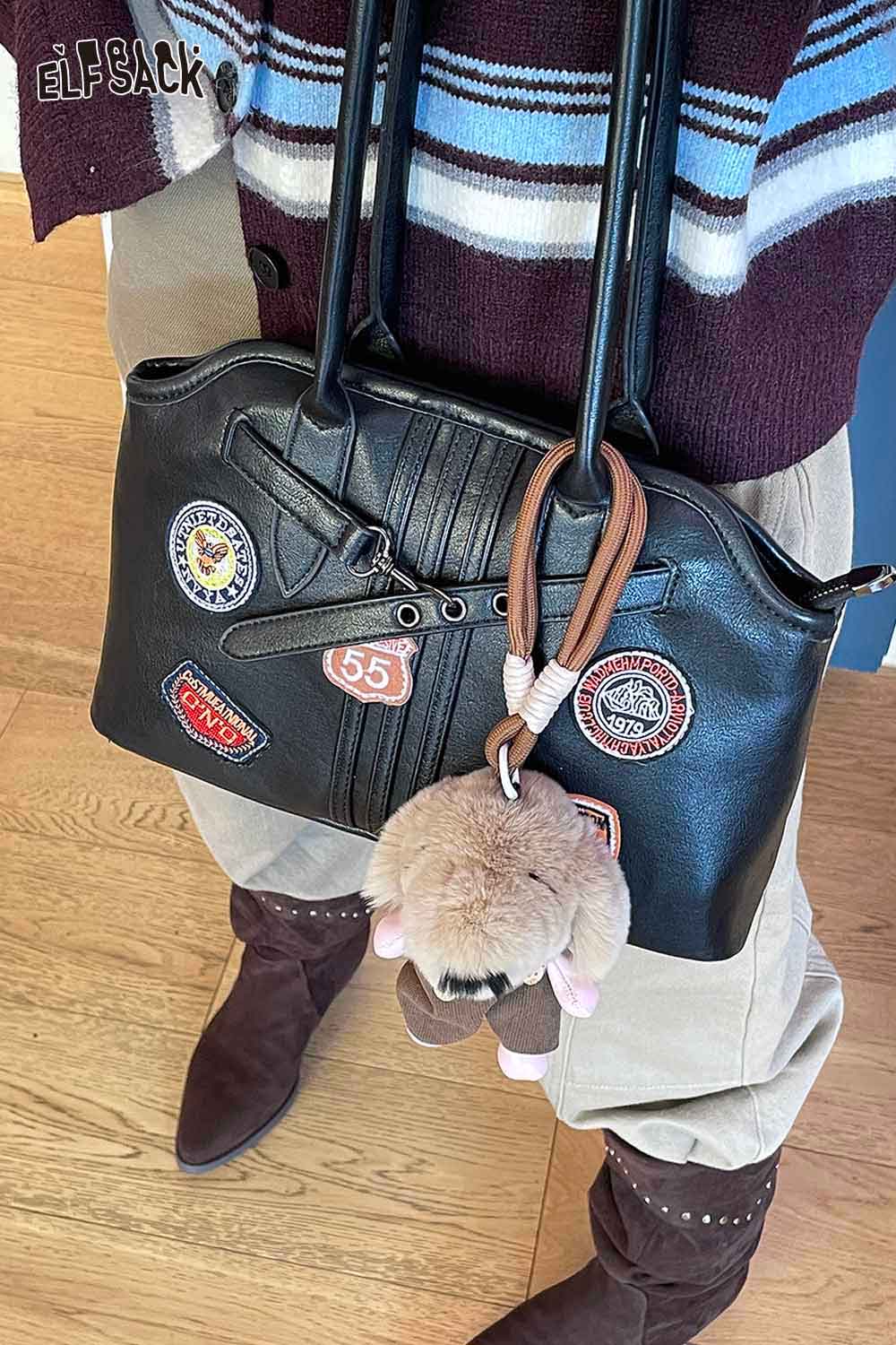 ELFSACK plush animal keychain attached to a stylish black handbag with patches