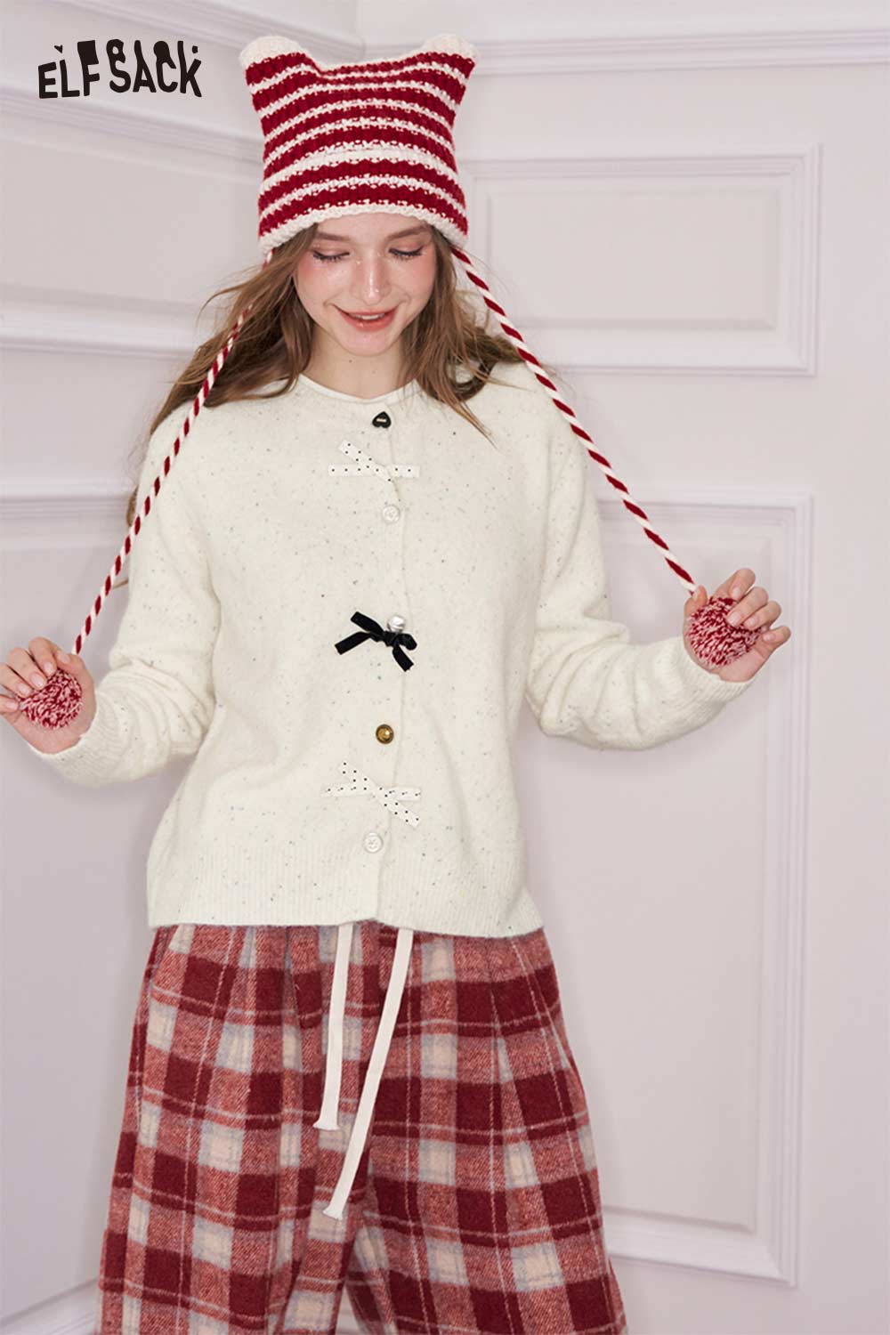 ELFSACK preppy 3D bow cardigan in cream displayed with a playful hat and plaid pants