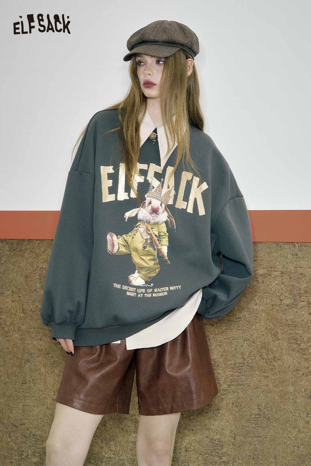 Model wearing ELFSACK PU leather pleated shorts paired with a graphic oversized sweatshirt and cap