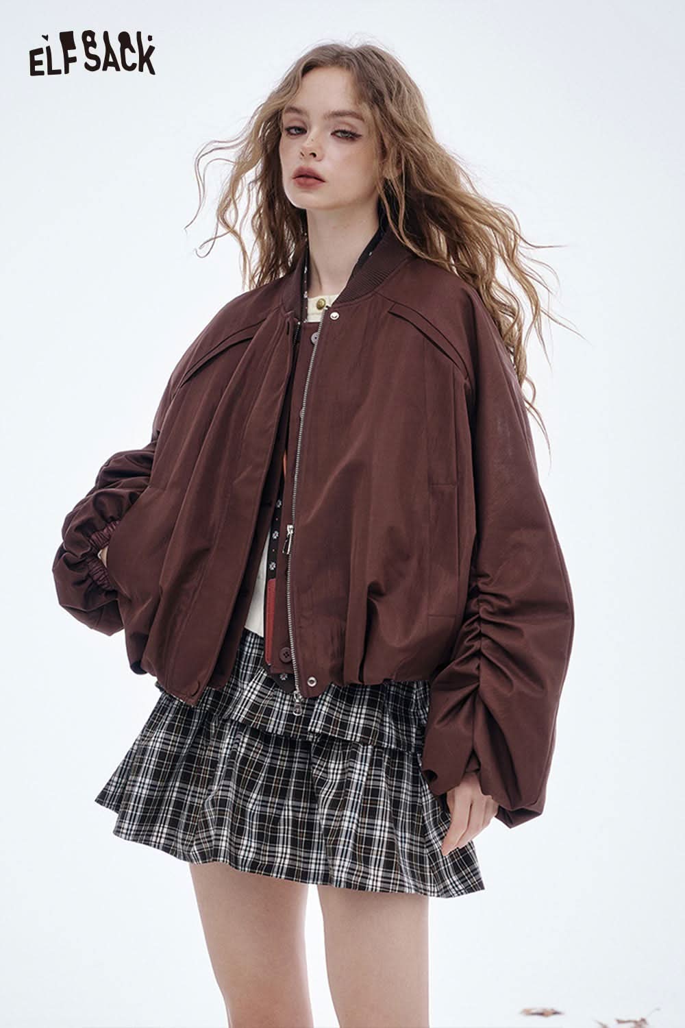 Model wearing a soft embroidered knit sweater from ELFSACK styled with a brown bomber jacket and plaid skirt