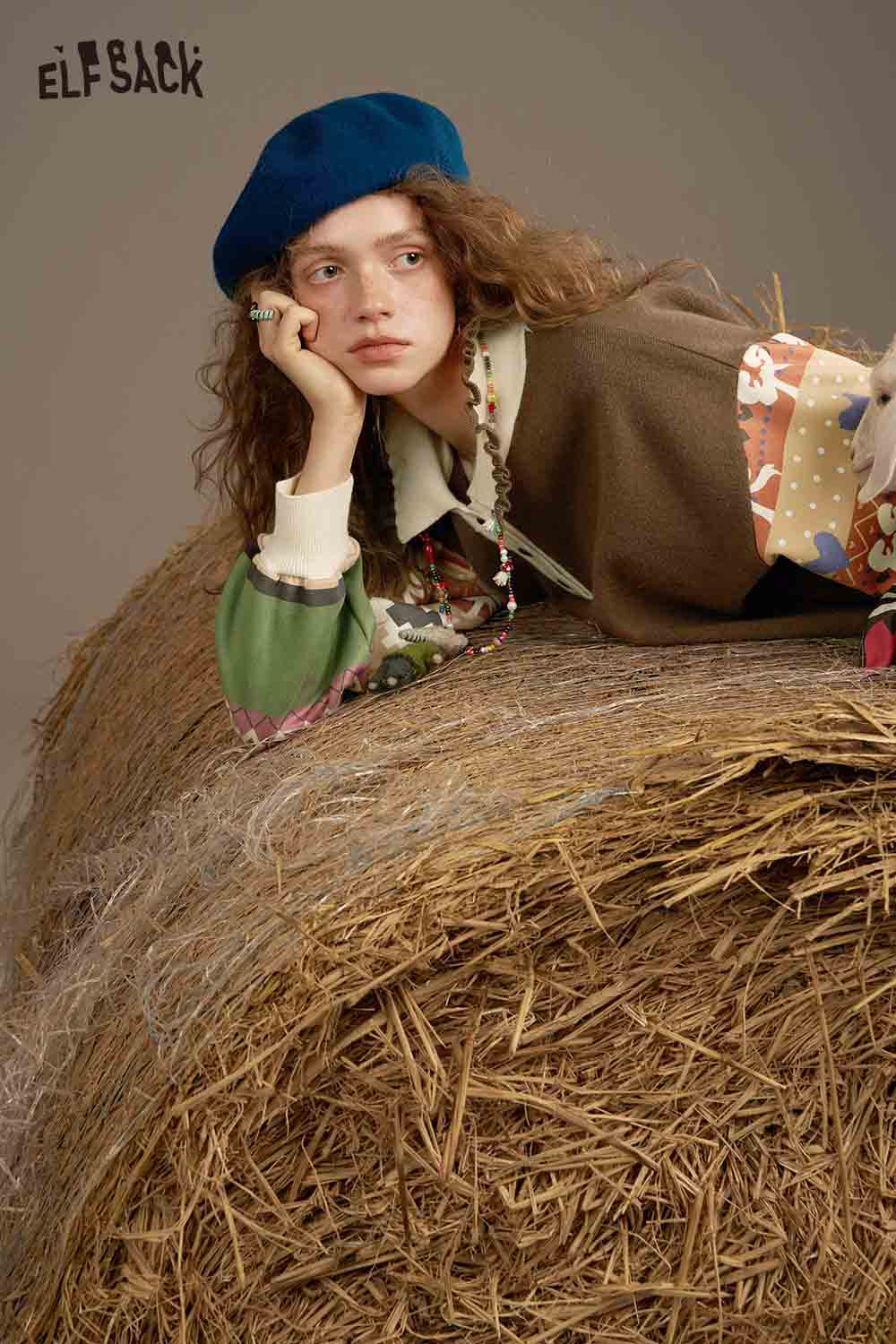 ELFSACK soft patchwork sleeve dress showcased by a model resting on hay, featuring colorful patterns.