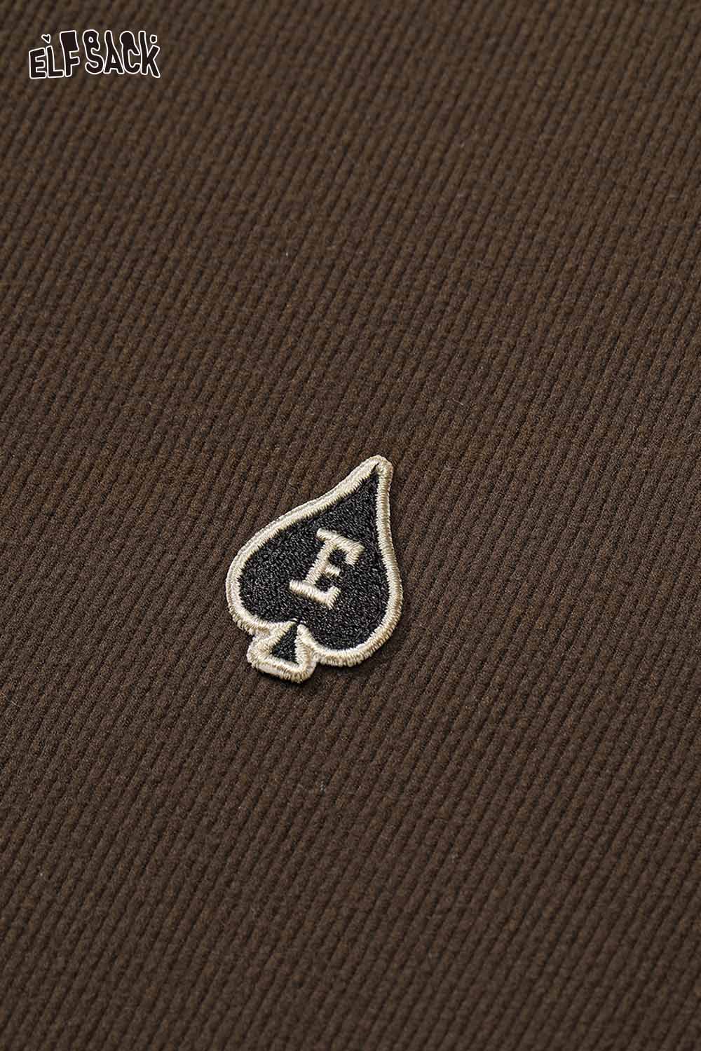 Close-up of ELFSACK soft spliced sleeve long sleeve tshirt featuring an embroidered logo on brown fabric