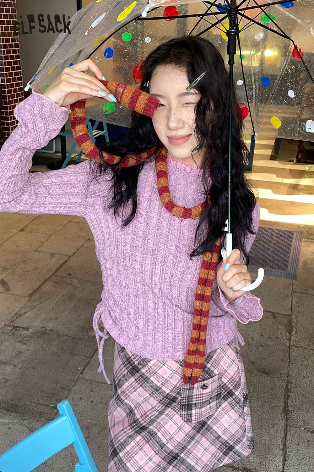 Woman wearing a pink sweater and skirt, showcasing a soft striped scarf for women draped around her neck