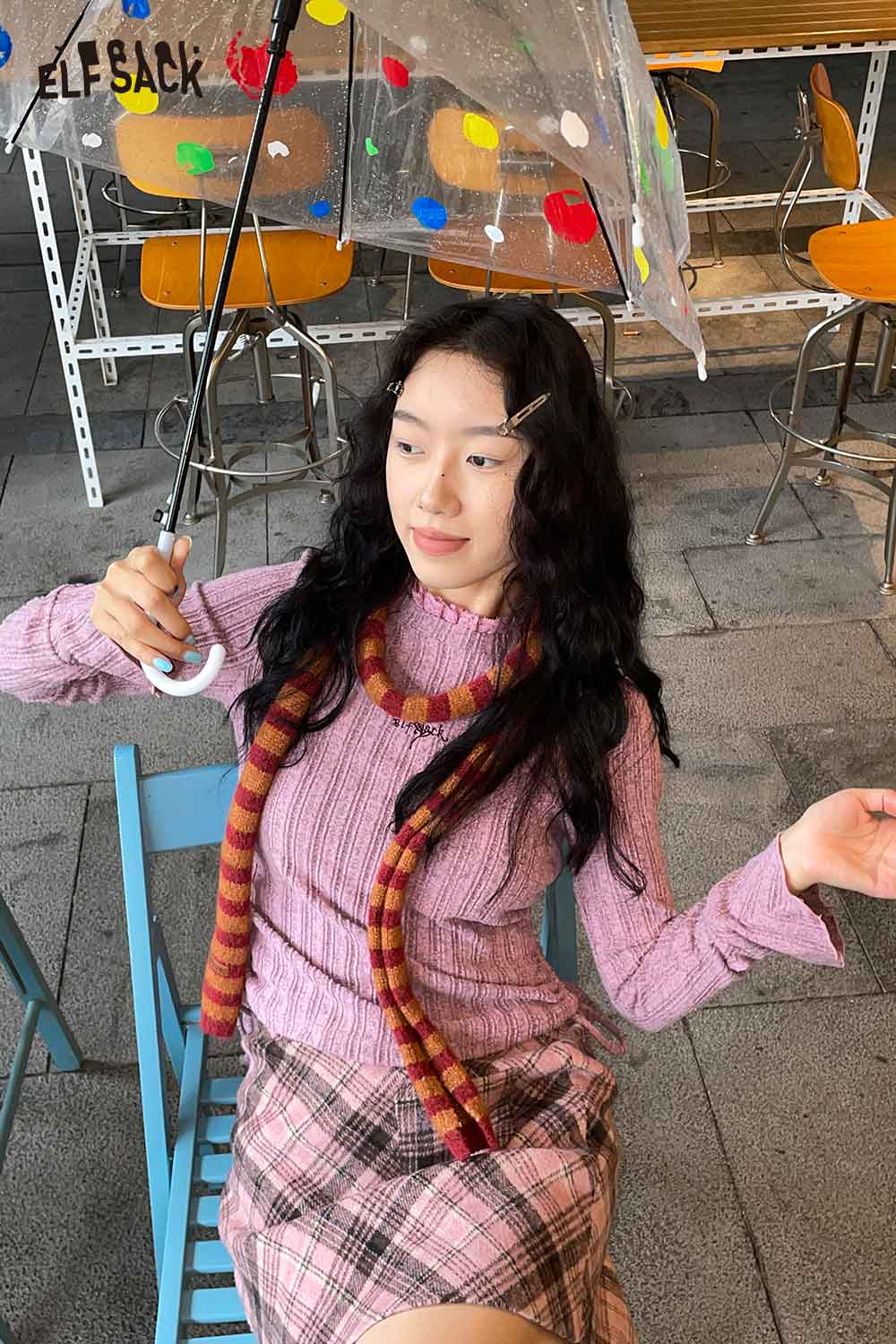 A woman wearing a pink ribbed sweater and holding a transparent umbrella, featuring a soft striped scarf for women