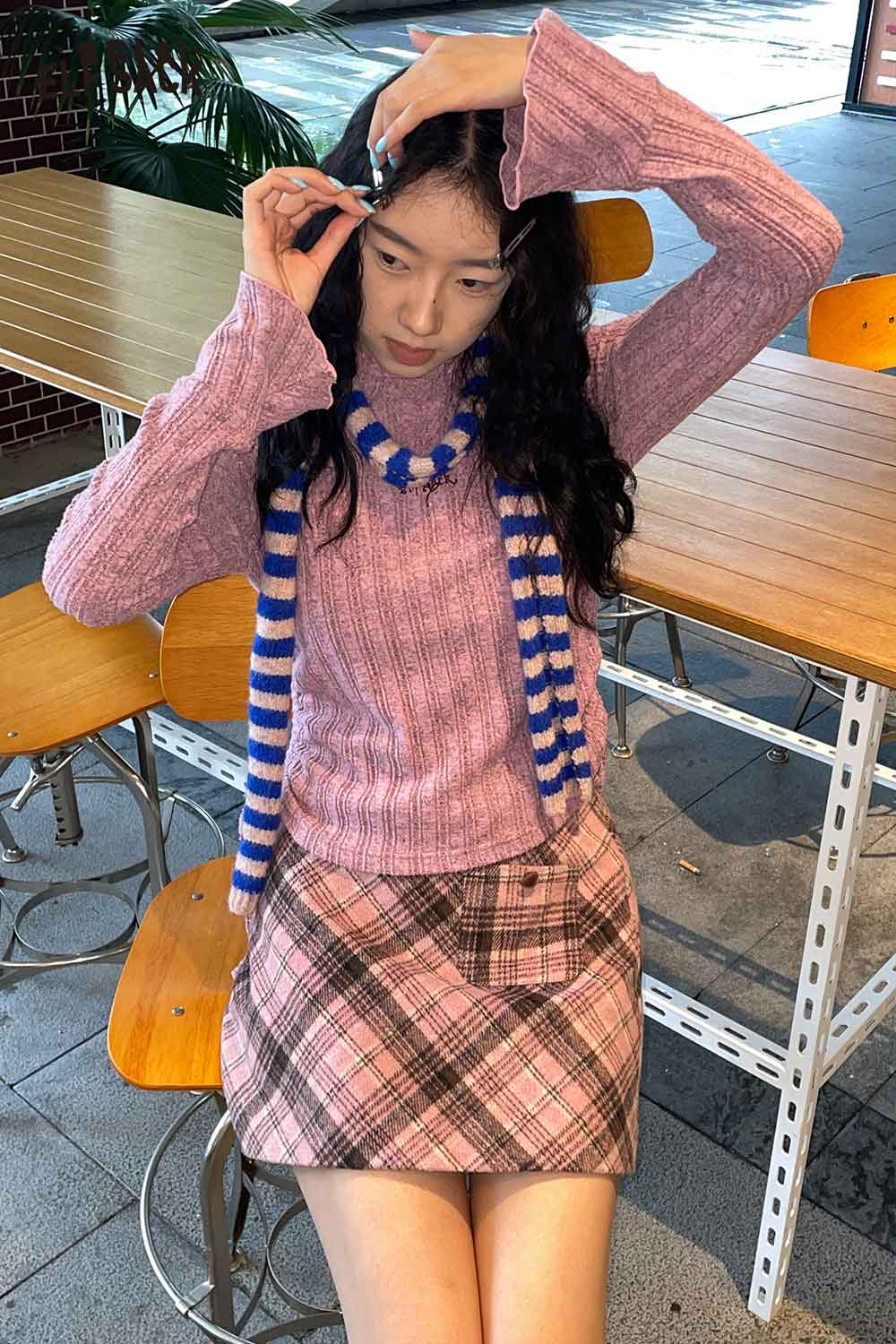 Chic woman wearing a soft striped scarf for women with a pink sweater and plaid skirt