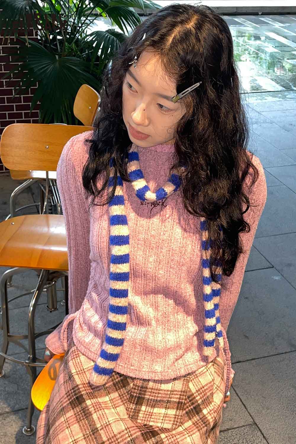 Stylish model wearing a soft striped scarf for women with a pink sweater and plaid skirt