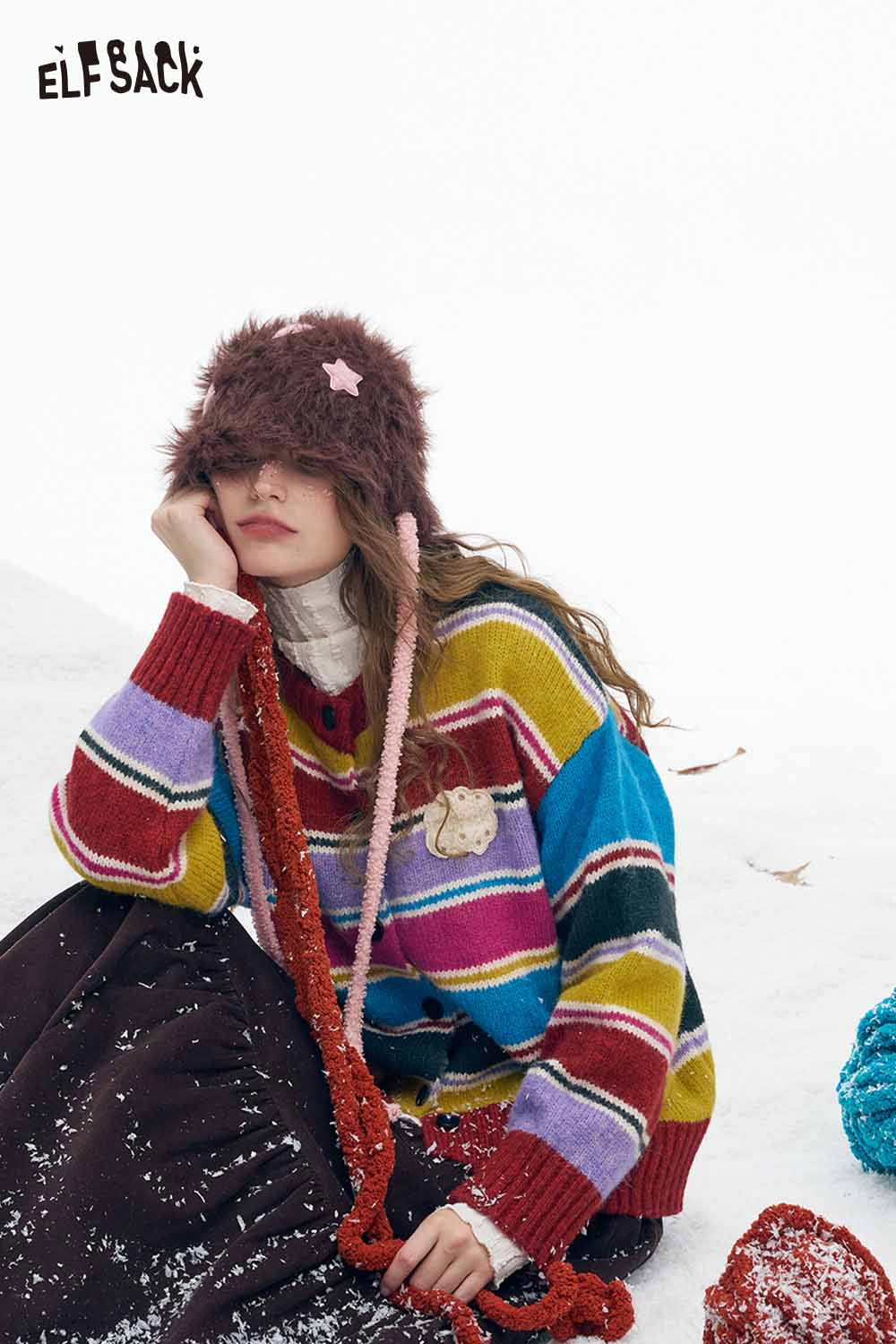 ELFSACK stripe embroidery button sweater in colorful stripes worn with a furry hat in a snowy setting