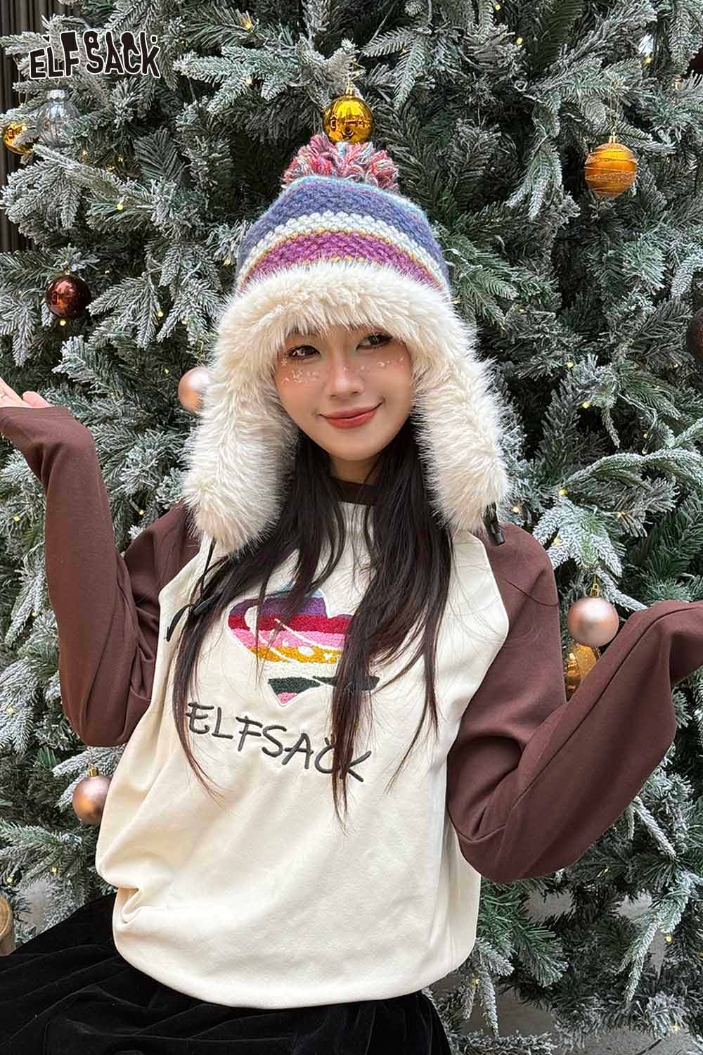 Young woman wearing a striped color block ear flap beanie and a stylish ELFSACK top in a festive setting