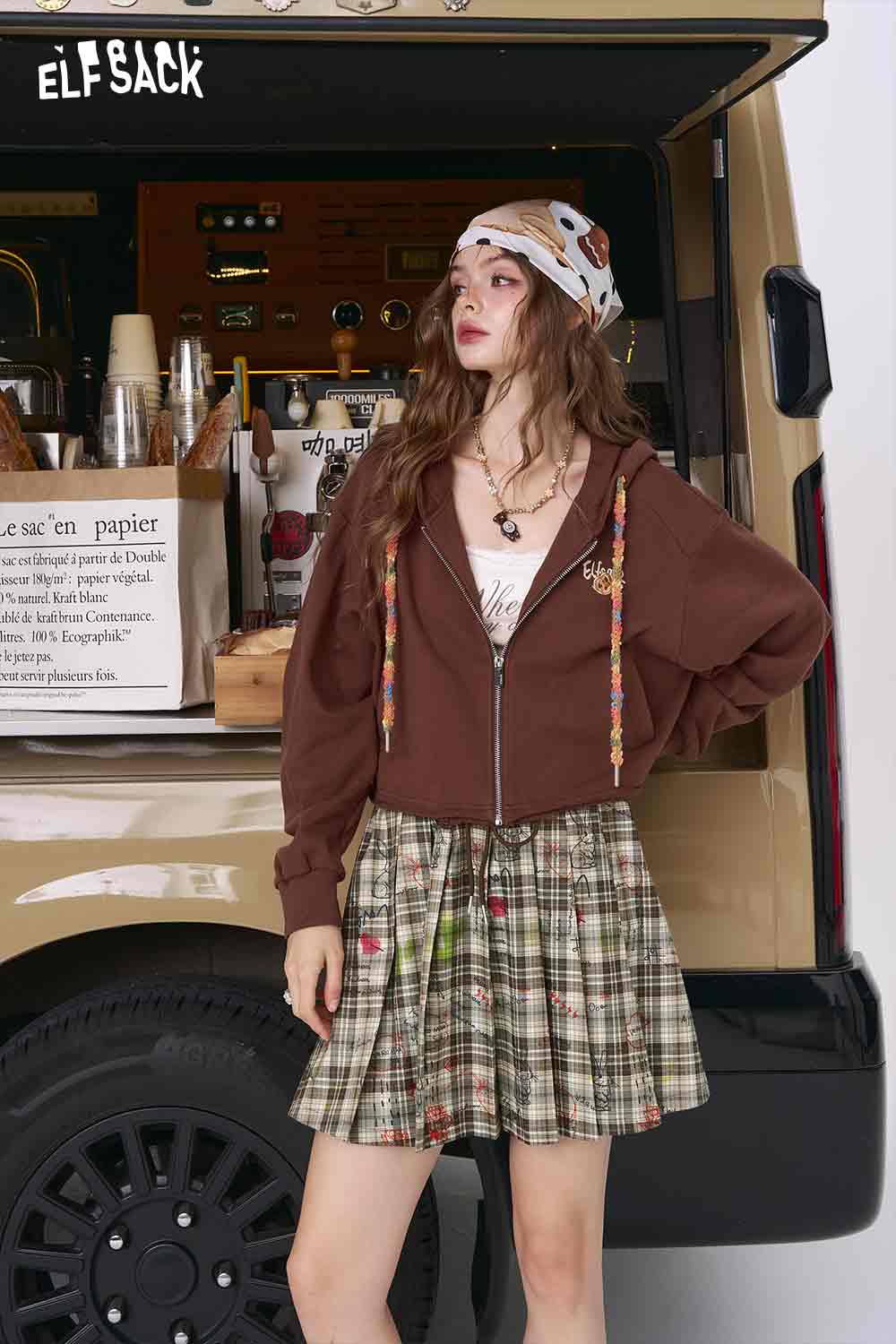 Model wearing college style plaid mini skirt in green beige tartan pleated style paired with brown zip hoodie
