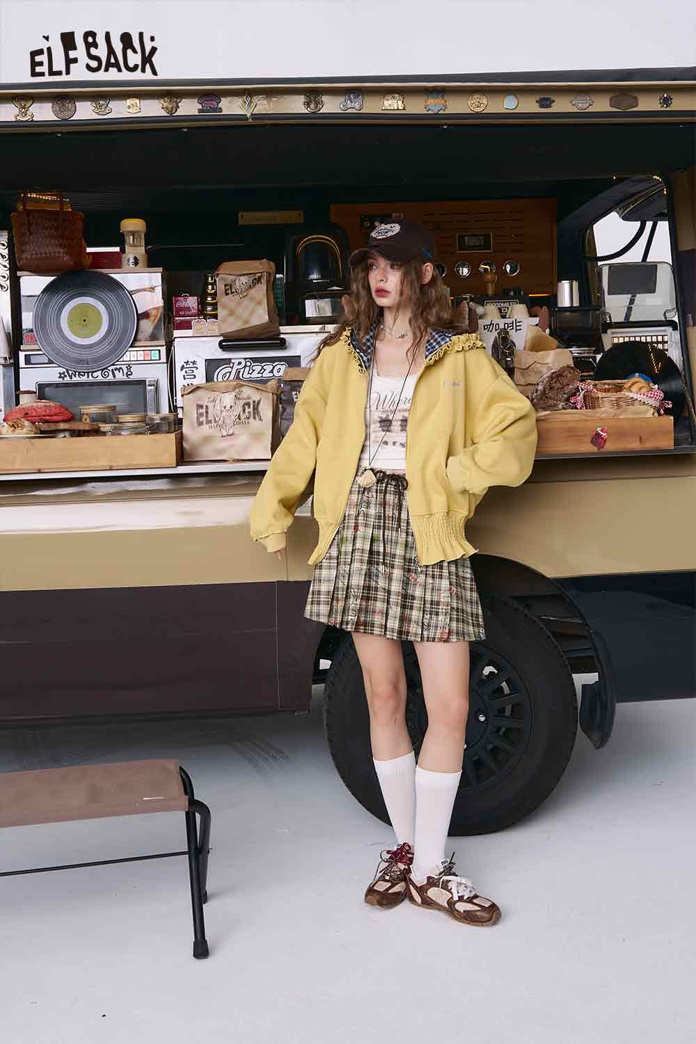 ELFSACK model wearing college style plaid mini skirt with yellow jacket knee socks and baseball cap at food truck