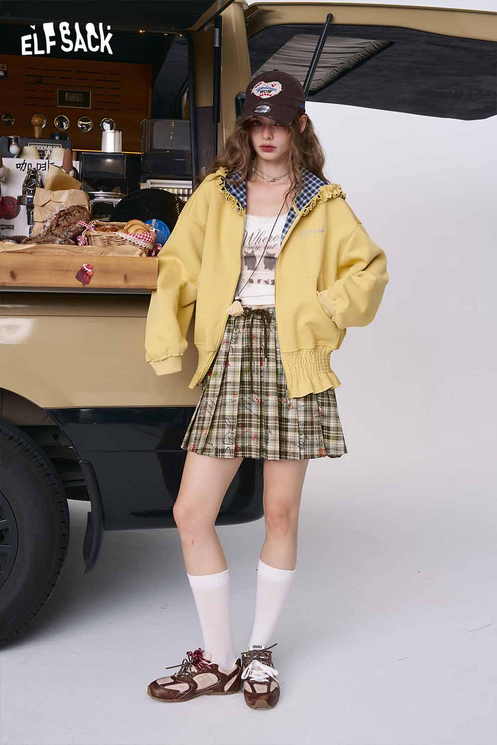 ELFSACK model wearing college style plaid mini skirt with oversized yellow jacket white knee socks and cap