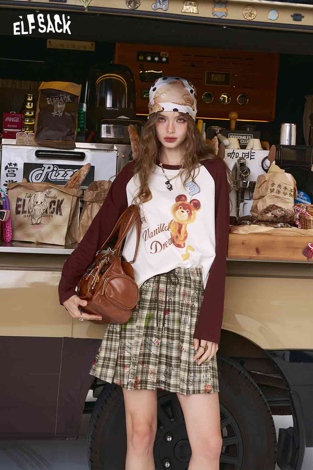 ELFSACK model wearing college style plaid mini skirt in green plaid paired with graphic raglan top and brown leather bag