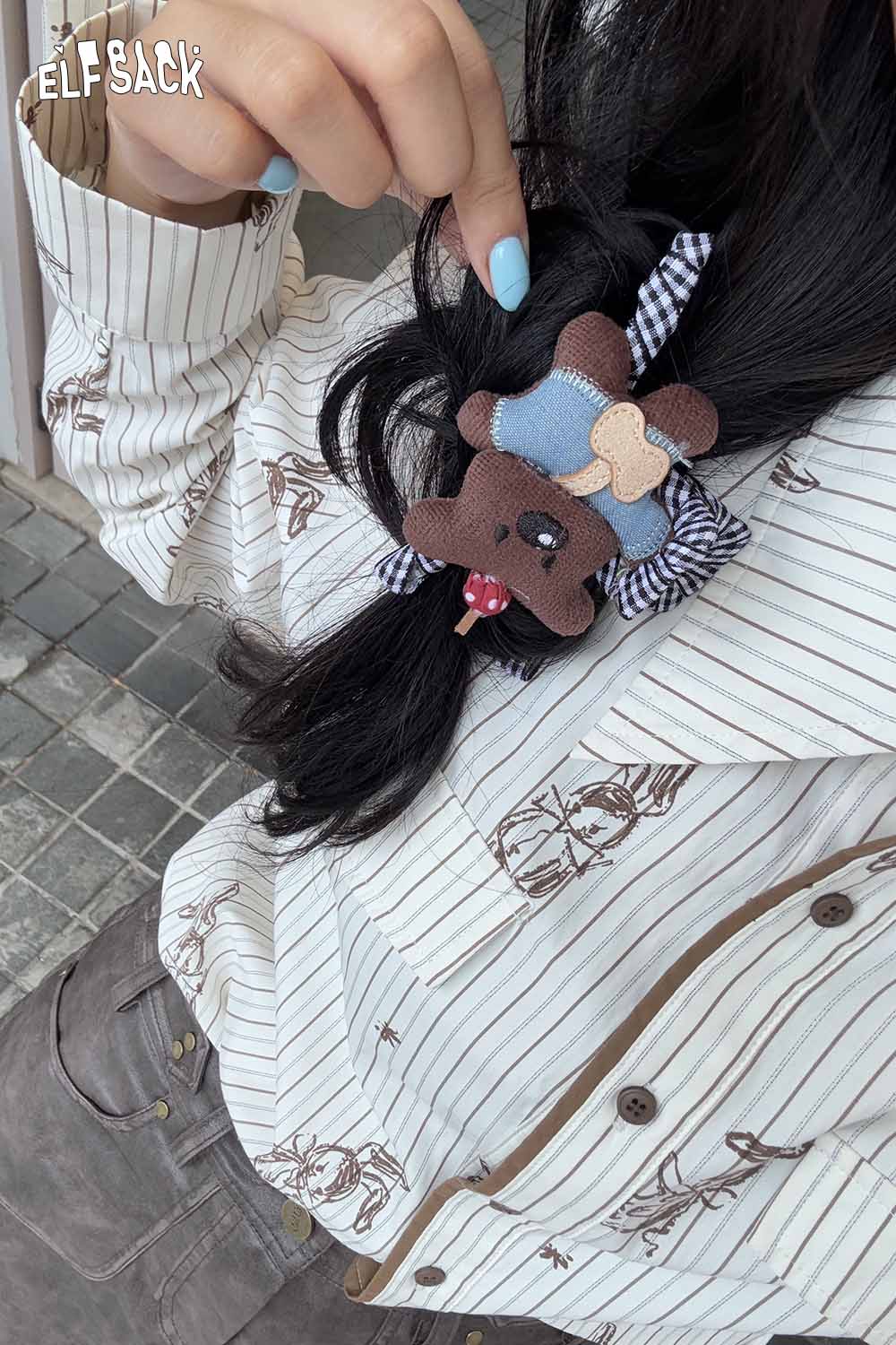 ELFSACK teddy bear hair clip attached to styled hair with a striped pattern shirt in the background