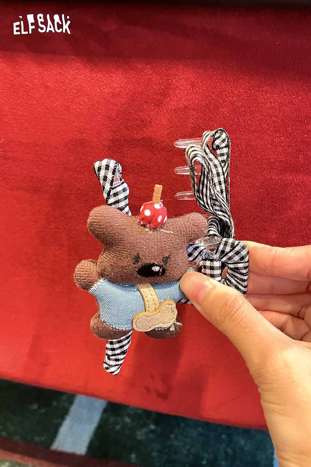 Cute ELFSACK teddy bear hair clip with checkered ribbons and a cherry on top for playful hairstyles