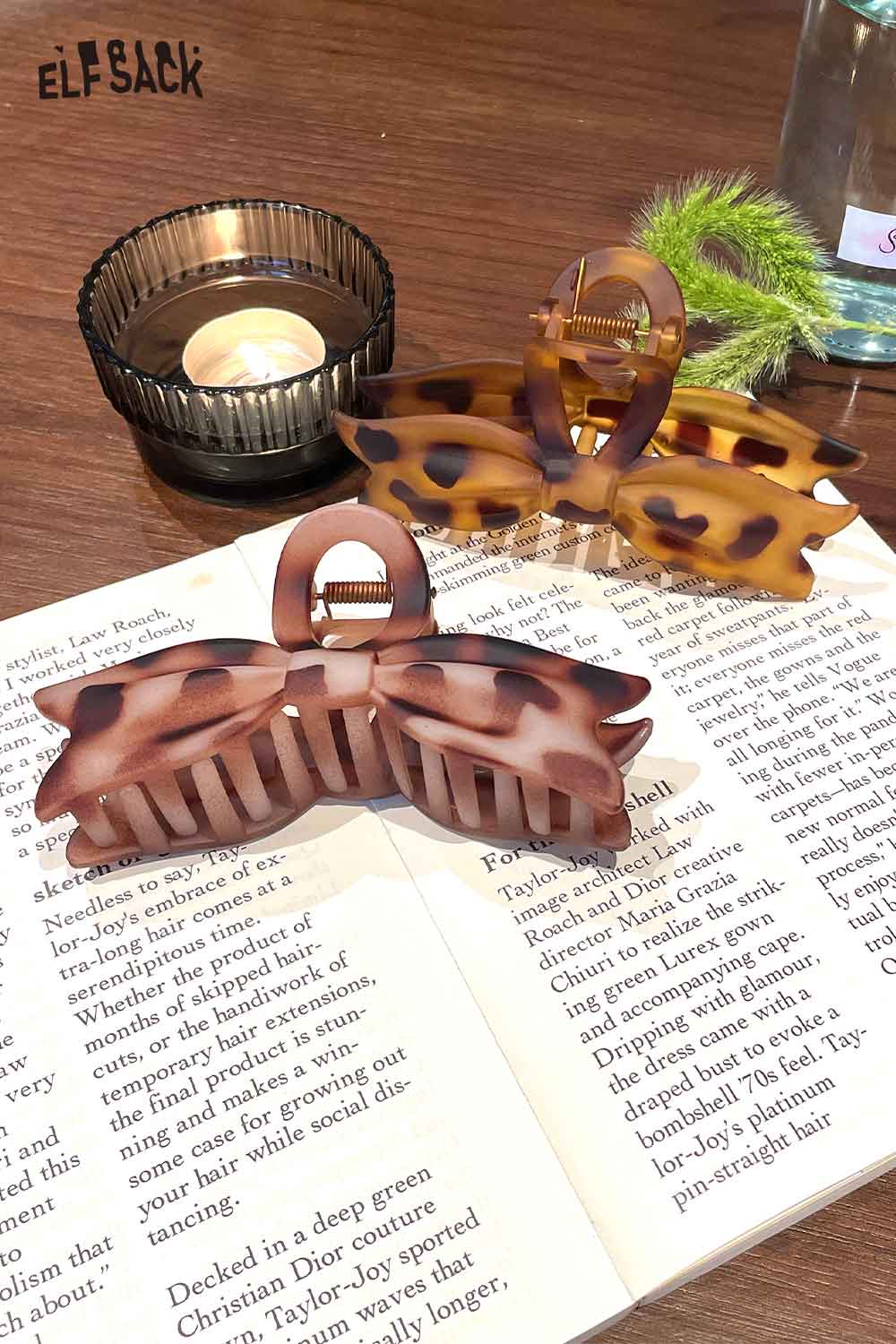 Two ELFSACK tortoiseshell bow hair claw clips displayed on a book with a candle