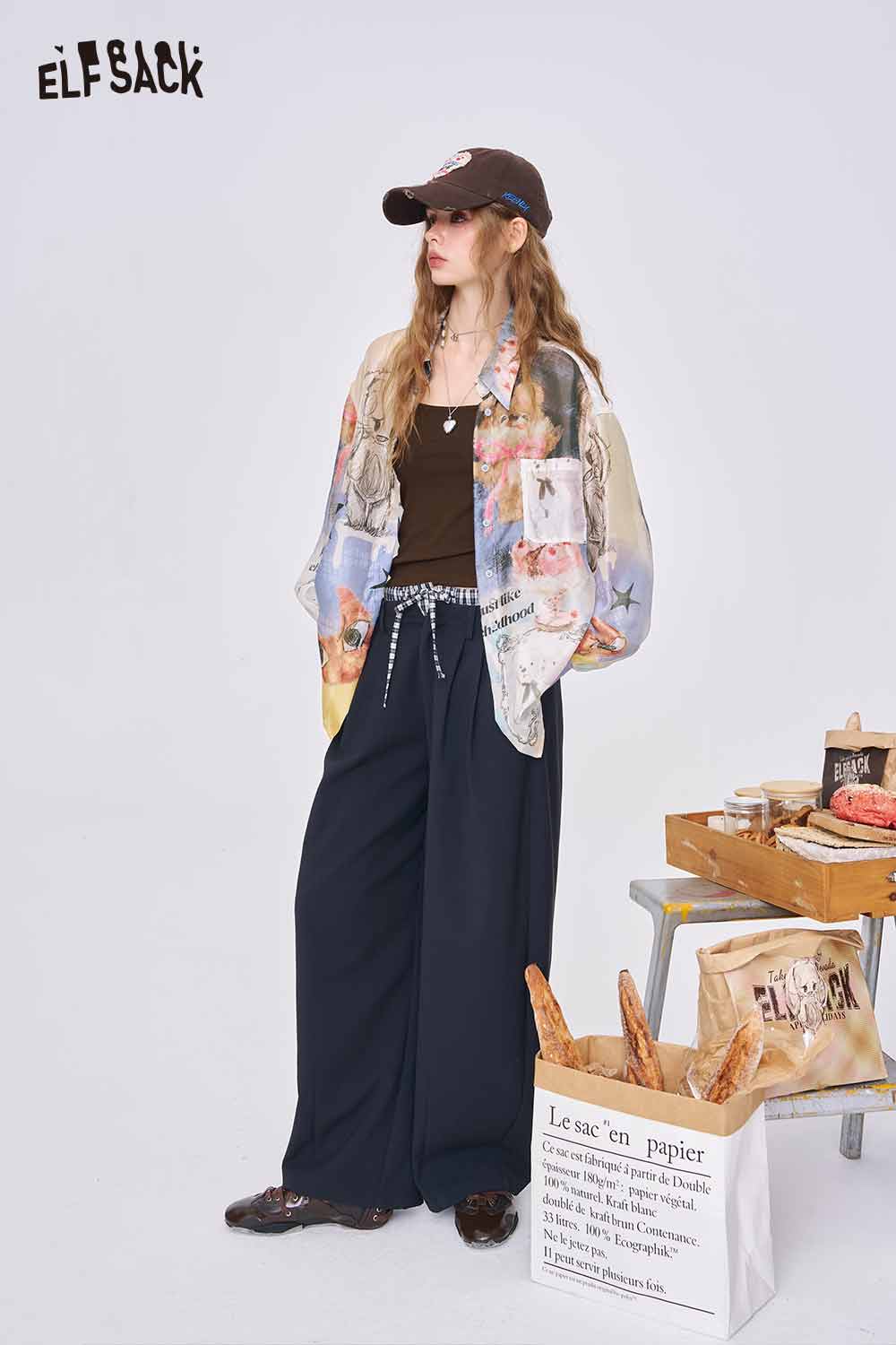 ELFSACK model wearing all over print long sleeve shirt over brown tank with wide leg navy pants