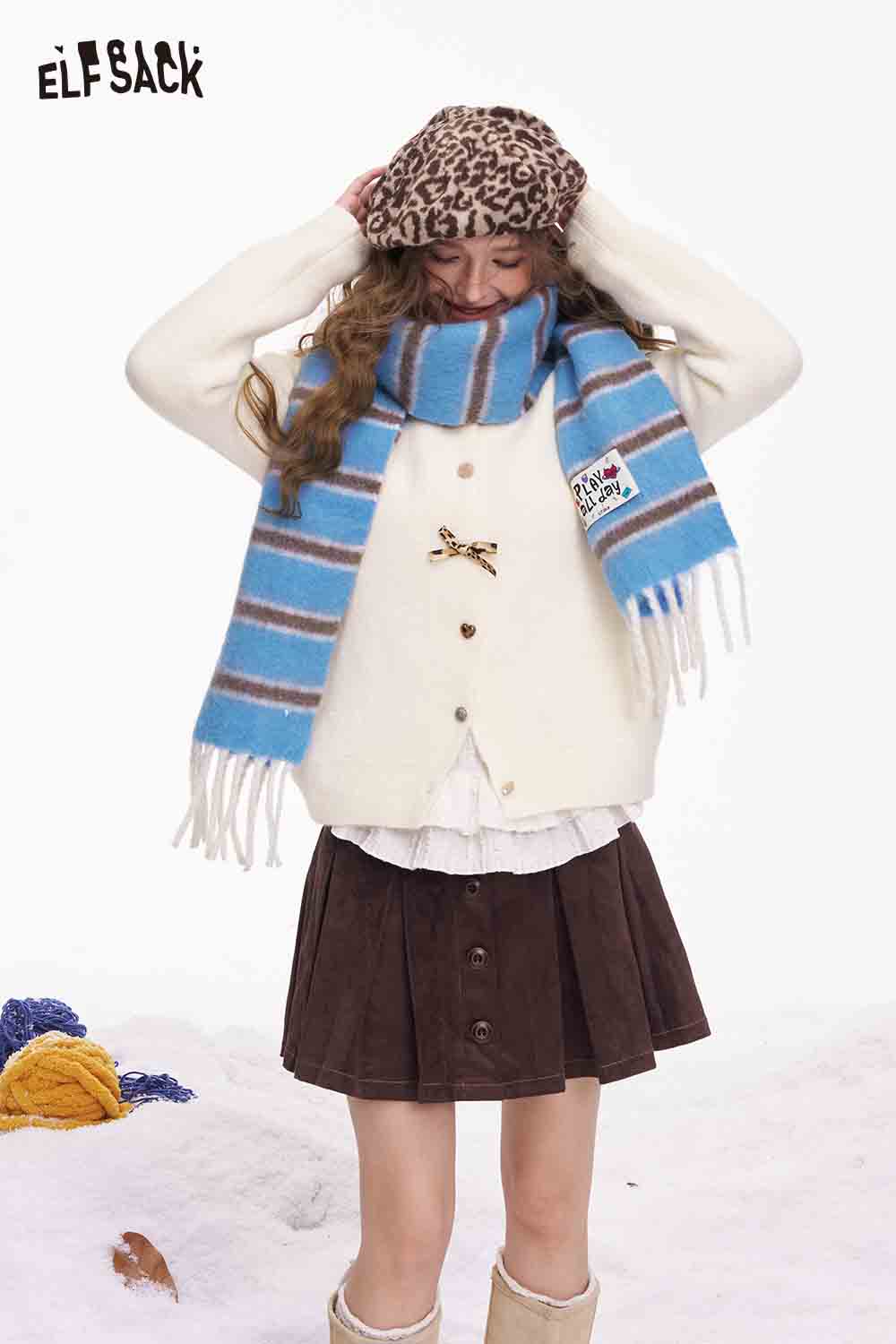 ELFSACK preppy striped fringe scarf in blue and brown, styled with a cream cardigan for a cozy winter look