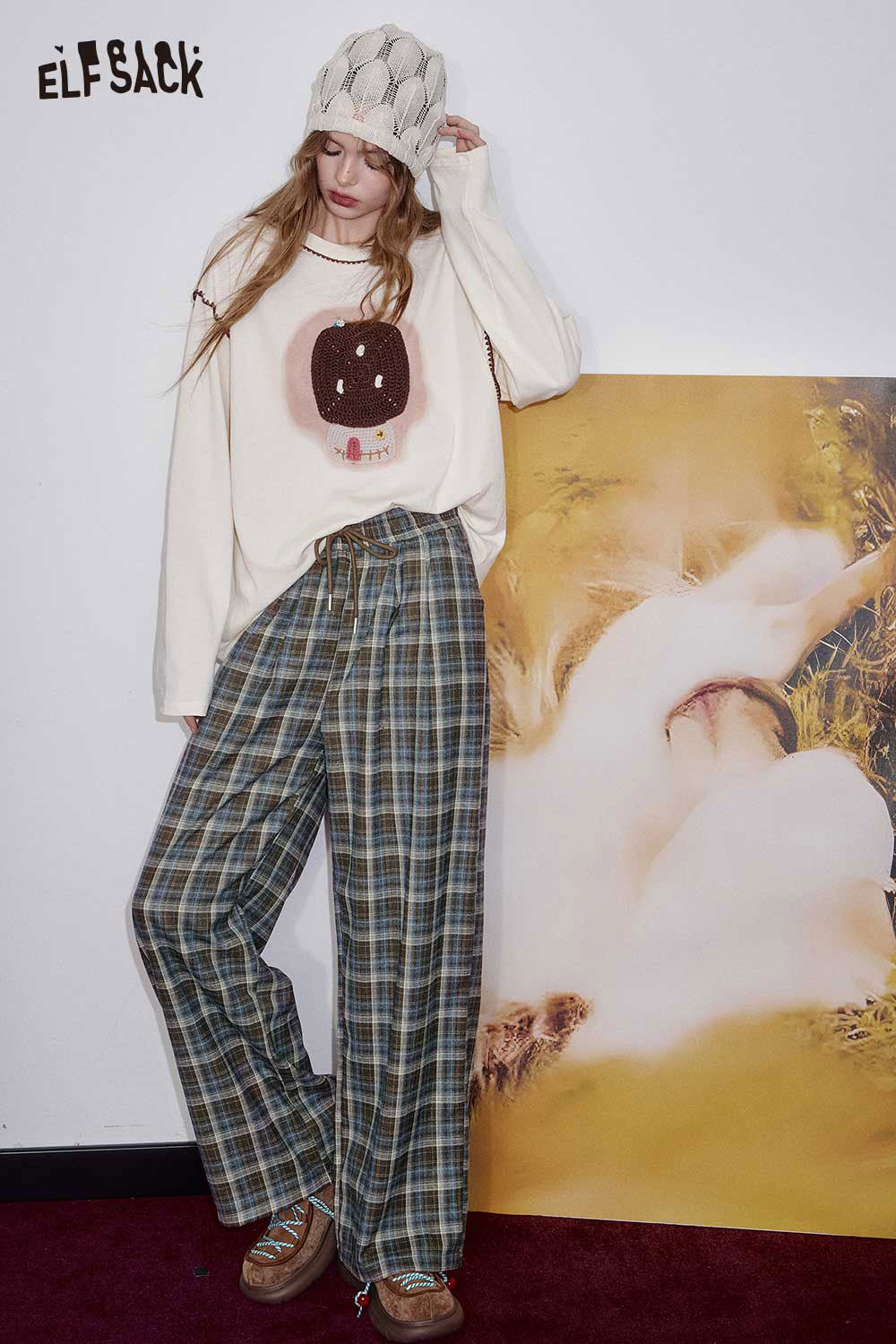 ELFSACK women's check pattern relaxed fit trousers paired with a playful graphic sweater and beanie.