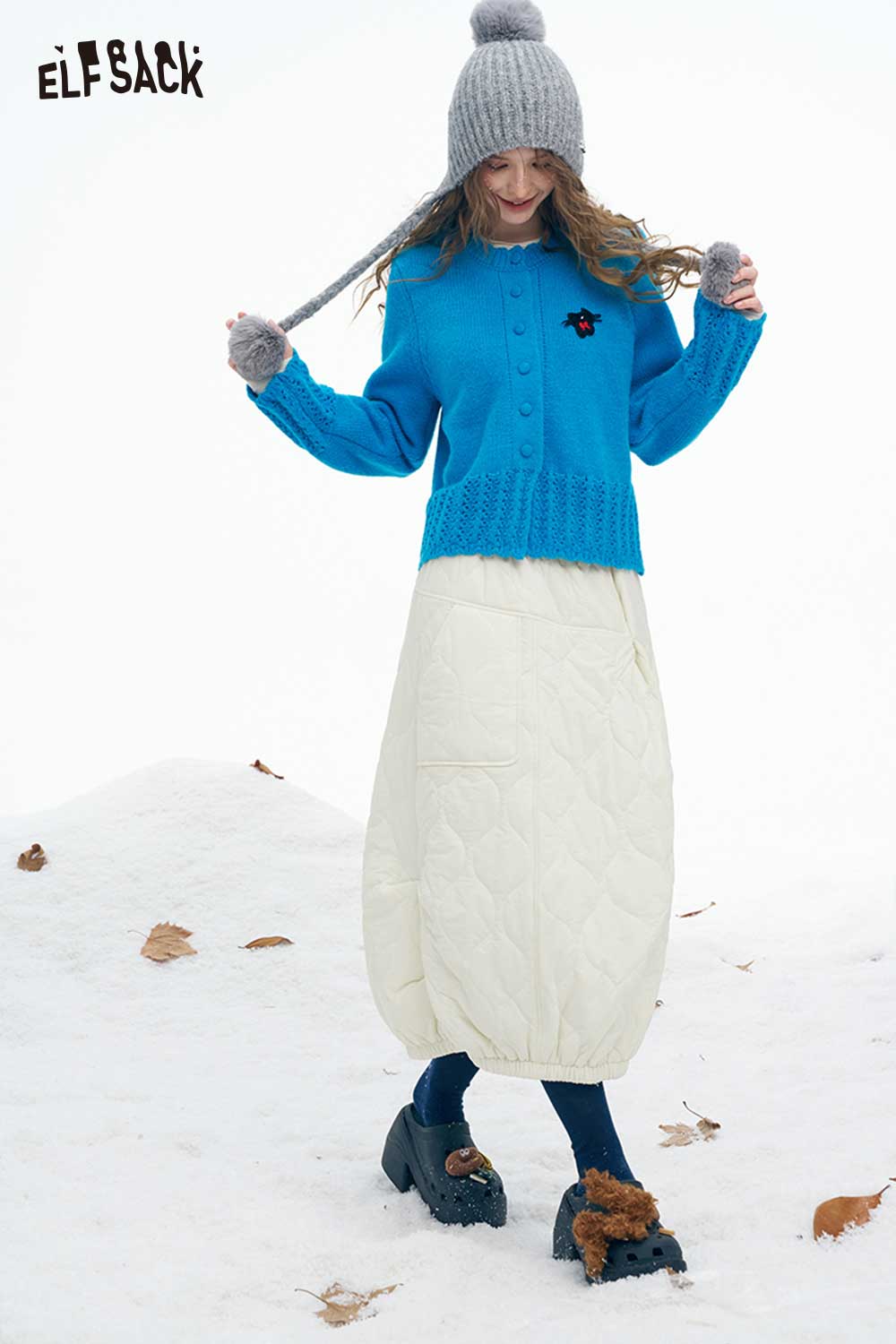 ELFSACK women's down half skirt in cream paired with a blue sweater in a snowy setting