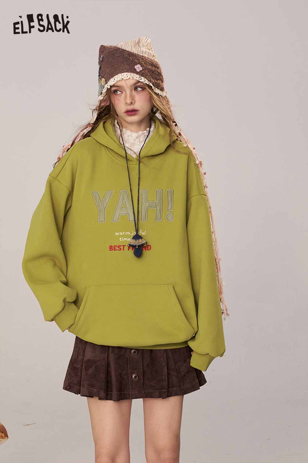 ELFSACK women's loose fit hooded sweatshirt in green with playful text, paired with a skirt and hat