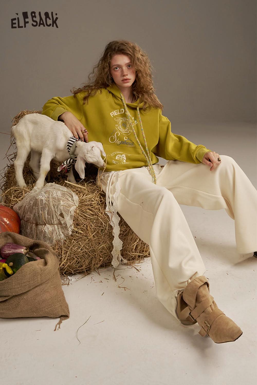 ELFSACK women's oversized print hoodie in green, styled with beige pants and seated with a goat