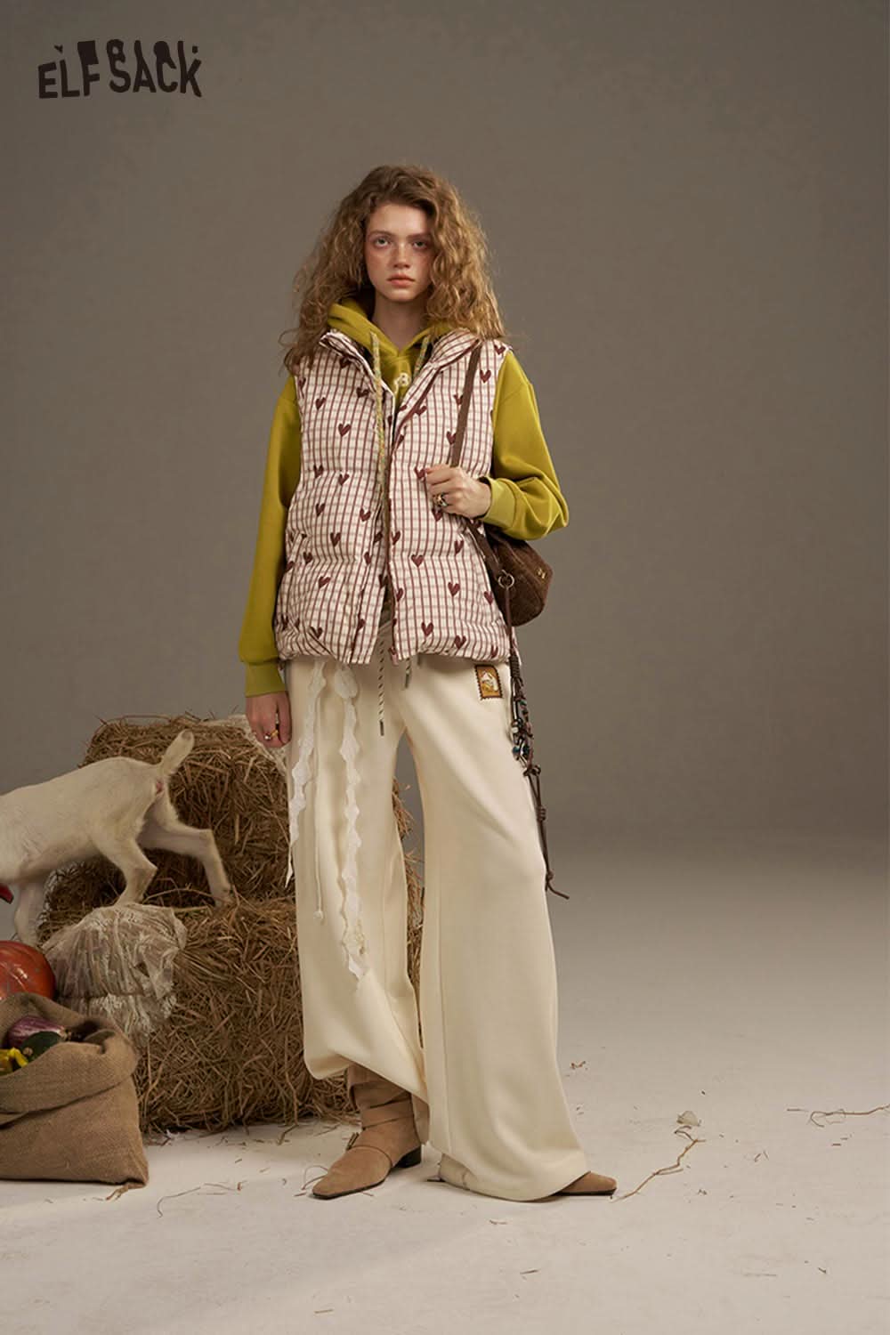 Stylish woman in an oversized print hoodie by ELFSACK paired with a puffy vest and wide-leg pants