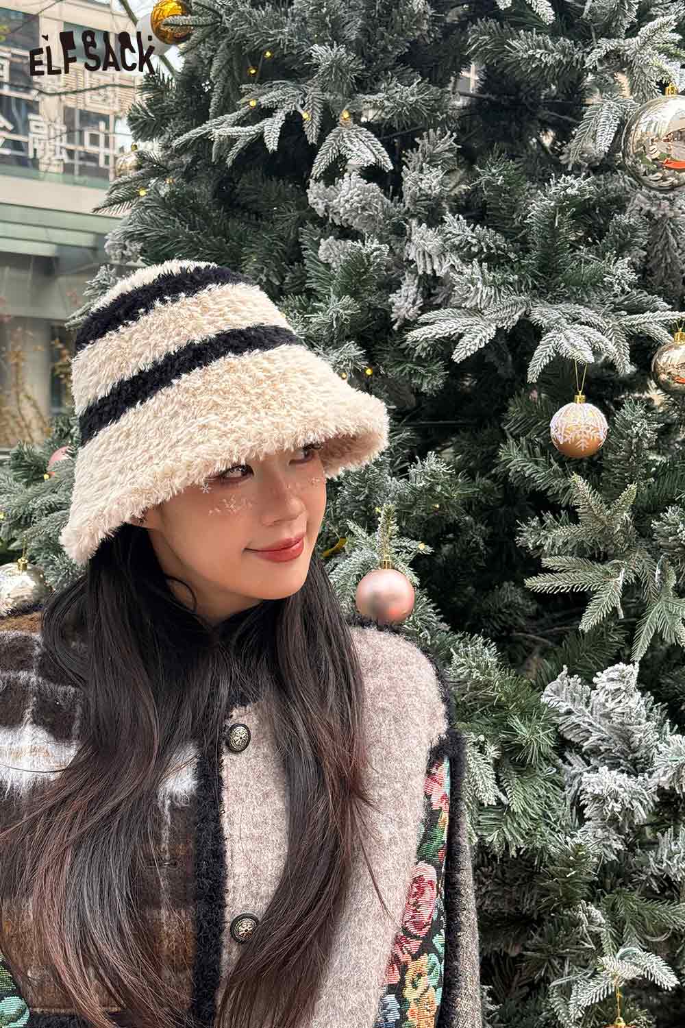 ELFSACK women's plush bucket hat in striped design worn by a model in front of a festive tree