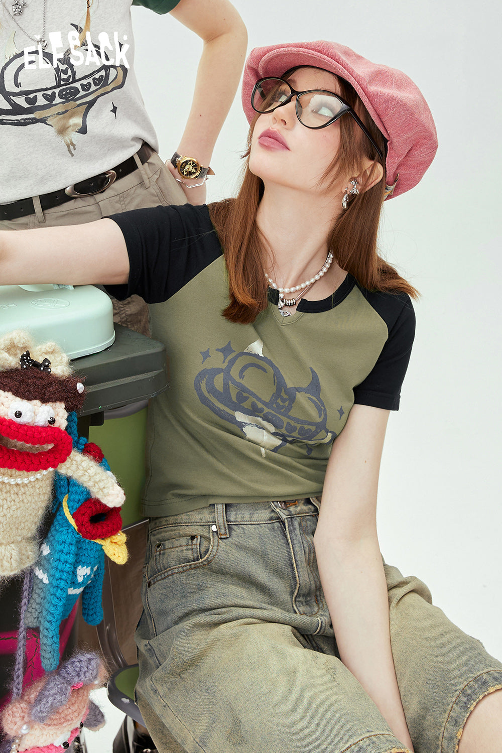 ELFSACK Y2K Heart Graphic olive green and black raglan T-shirt worn by woman with pink hat and glasses