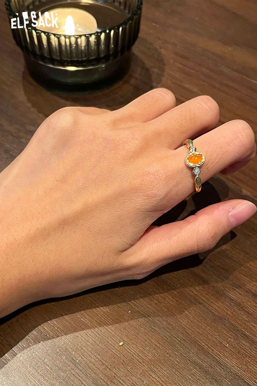Hand wearing an ELFSACK zirconia gemstone copper ring with colorful stones, set against a cozy candlelight.