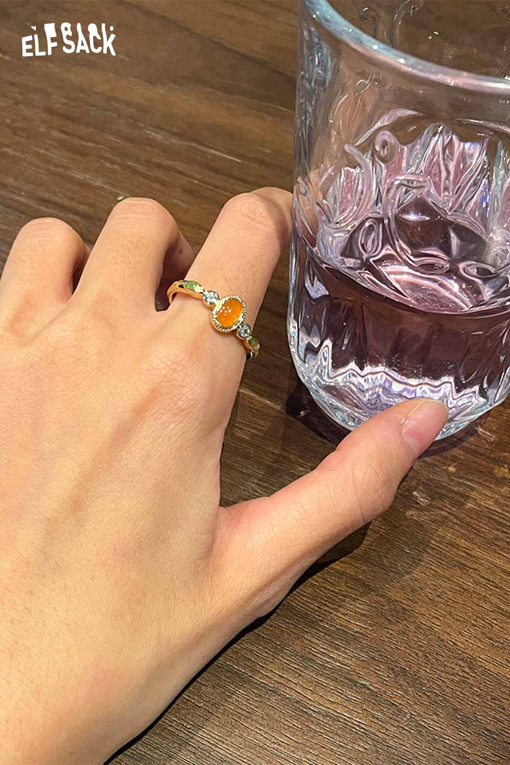 ELFSACK zirconia gemstone copper ring worn on hand next to a glass of water